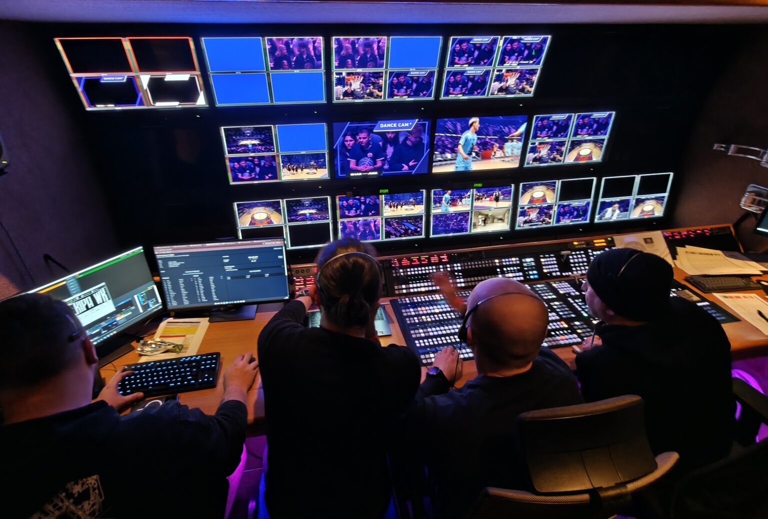OB van production gallery during a live basketball broadcast – director and crew at the vision mixer, monitor wall with camera feeds